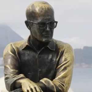 Estátua de Carlos Drummond de Andrade na Praia de Copacabana. O poeta está sentado num banco da orla.