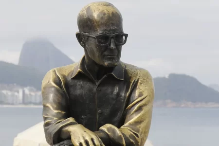 Estátua de Carlos Drummond de Andrade na Praia de Copacabana. O poeta está sentado num banco da orla.